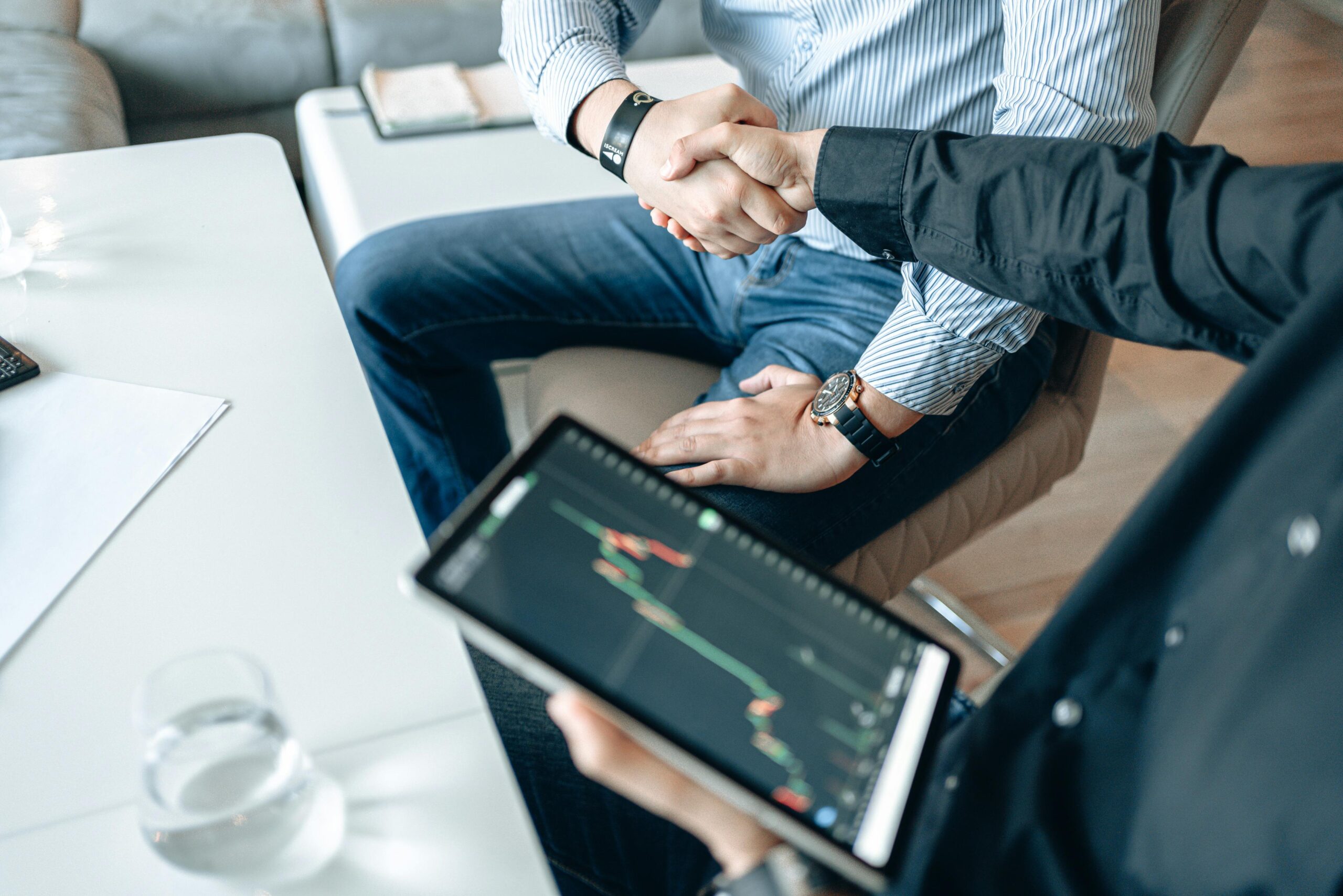 Business professionals shaking hands with a tablet displaying financial graphs.