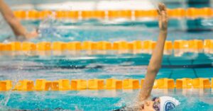 A determined child swimmer performing the backstroke in an indoor swimming pool competition.
