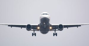 A commercial airliner captured head-on, preparing to land against a cloudy sky.